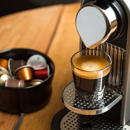Copenhagen, Denmark - July 8, 2014: Freshly brewed espresso in glass standing on silver Nespresso coffe machine. Blurred background with Nespresso capsules in black bowl.